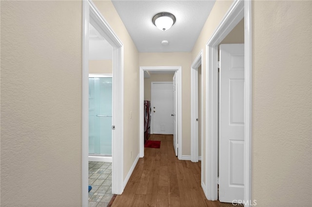 hallway with baseboards, a textured wall, washer / dryer, and wood finished floors