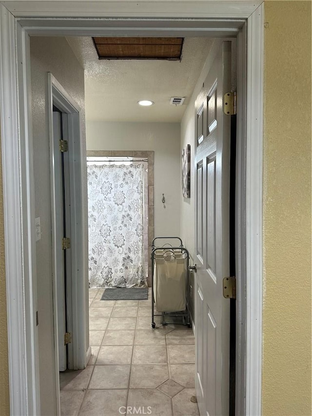 corridor with light tile patterned floors, a textured ceiling, and visible vents