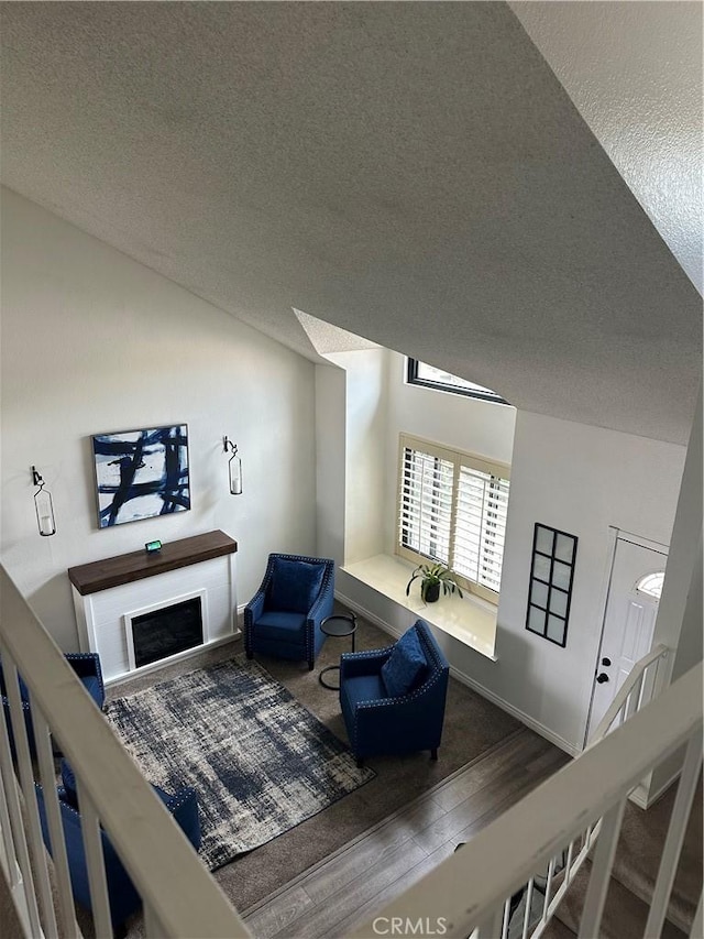 living room with a fireplace, vaulted ceiling, a textured ceiling, and wood finished floors