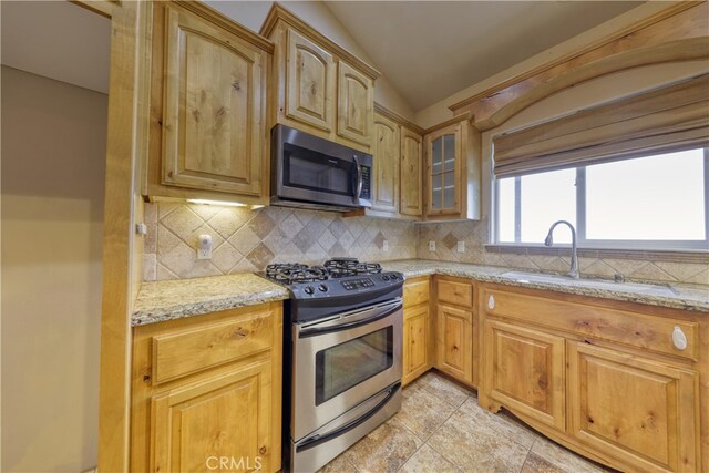 kitchen with a sink, decorative backsplash, light stone countertops, and stainless steel appliances