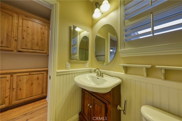 bathroom with vanity, a decorative wall, toilet, a wainscoted wall, and wood finished floors