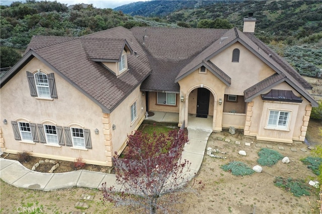 view of front of home with a mountain view, roof with shingles, stucco siding, and a chimney