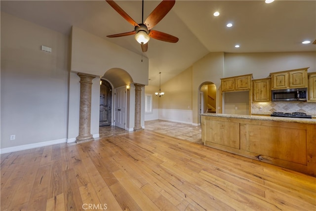kitchen with light wood-style floors, ornate columns, stainless steel microwave, arched walkways, and ceiling fan with notable chandelier
