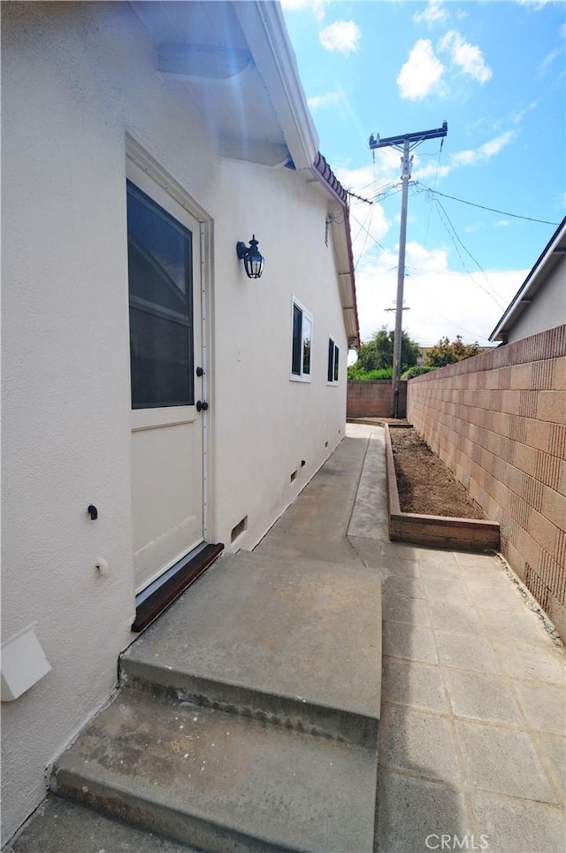 view of exterior entry with fence, a patio area, and stucco siding