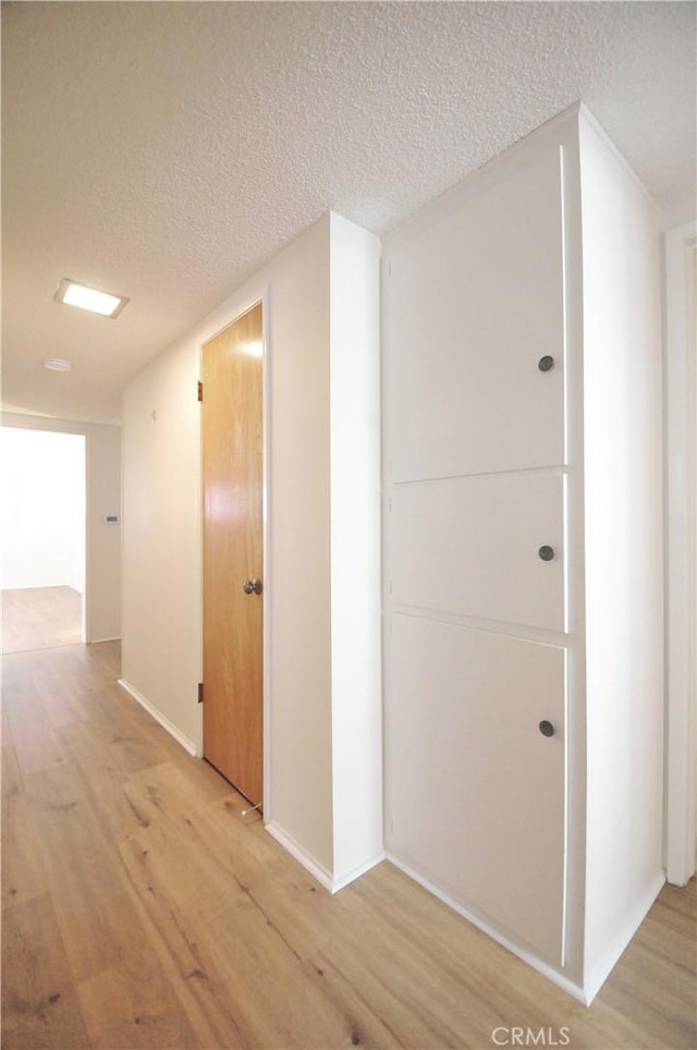 hallway with a textured ceiling, baseboards, and light wood-type flooring