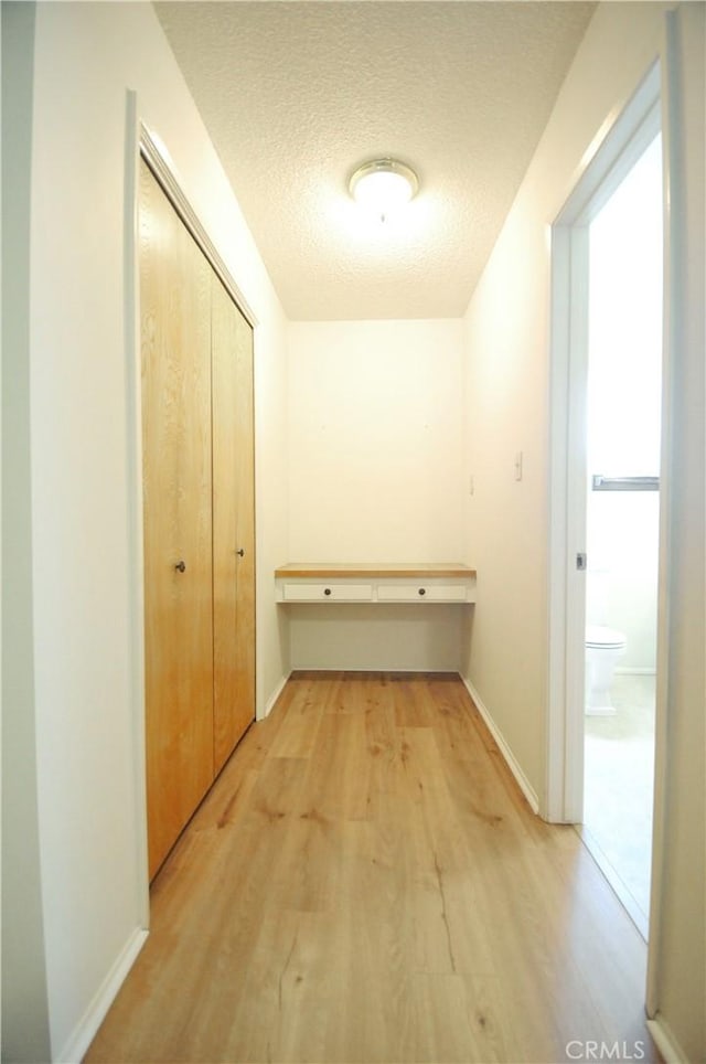 corridor featuring baseboards, a textured ceiling, and light wood finished floors