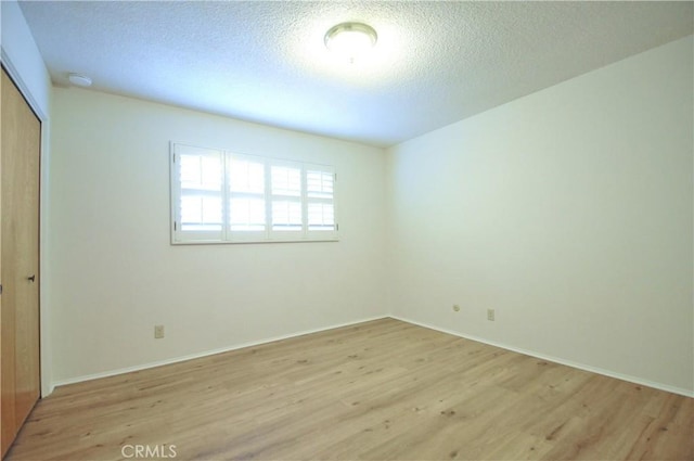 unfurnished bedroom with light wood-style floors, baseboards, a closet, and a textured ceiling
