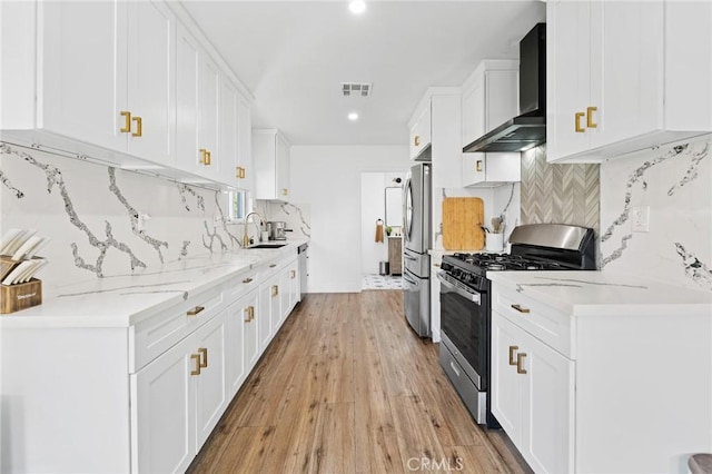 kitchen featuring wall chimney range hood, light wood-type flooring, a sink, backsplash, and stainless steel appliances