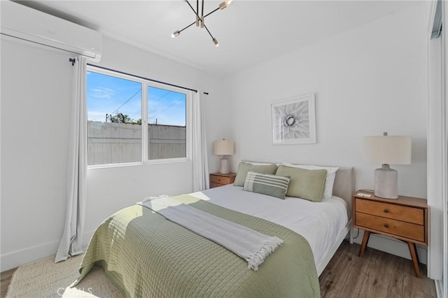 bedroom with wood finished floors, baseboards, a wall unit AC, and a notable chandelier