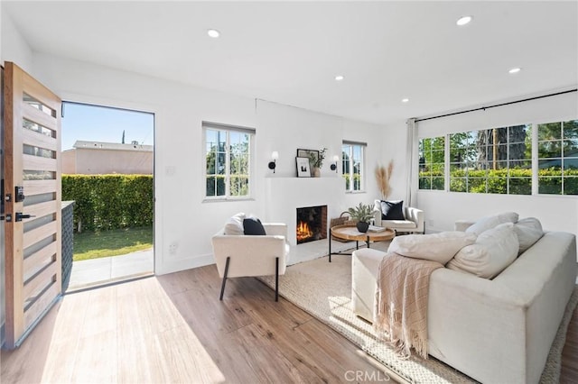 living area featuring recessed lighting, plenty of natural light, wood finished floors, and a warm lit fireplace