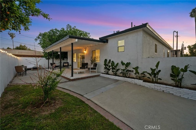 back of property at dusk featuring a patio, a fenced backyard, and stucco siding