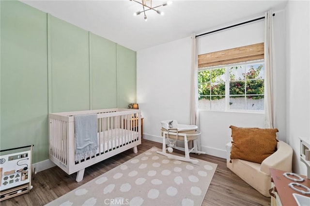 bedroom featuring an inviting chandelier, baseboards, a crib, and wood finished floors