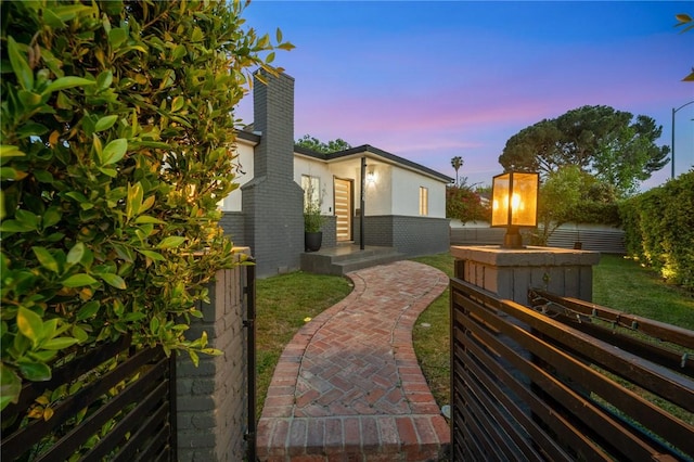 property exterior at dusk featuring brick siding, fence, and a chimney