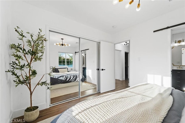 bedroom with an inviting chandelier, a barn door, baseboards, wood finished floors, and a closet