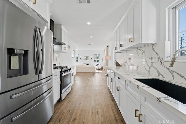 kitchen with white cabinets, appliances with stainless steel finishes, light stone counters, a sink, and open floor plan