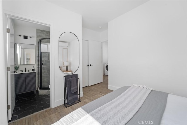 bedroom with washer / dryer, wood finished floors, and connected bathroom