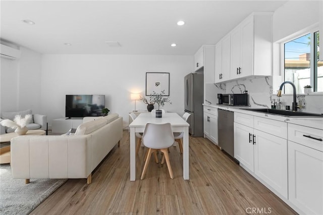 kitchen featuring an AC wall unit, a sink, light wood-style floors, and stainless steel appliances