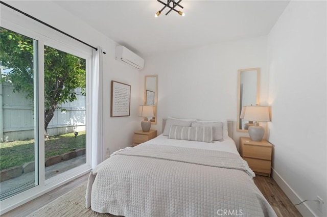 bedroom with wood finished floors, baseboards, and a wall mounted AC