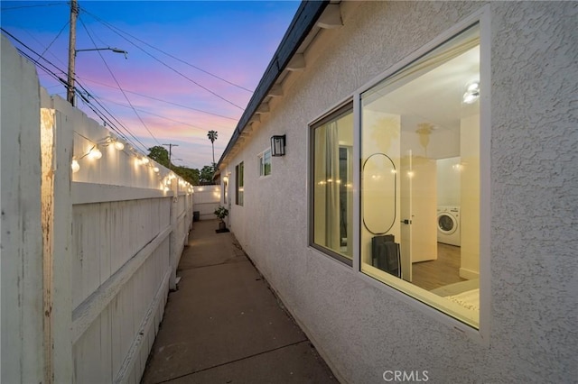 property exterior at dusk with washer / dryer, stucco siding, and fence