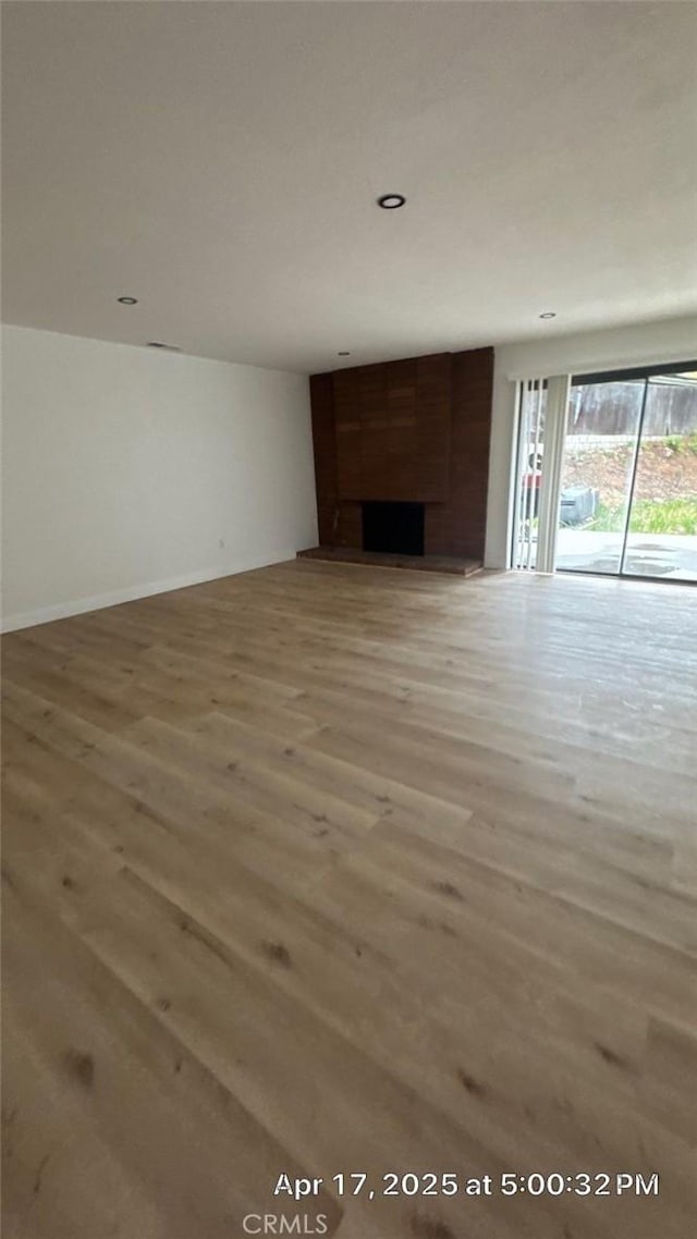 unfurnished living room featuring recessed lighting, a large fireplace, baseboards, and light wood-type flooring