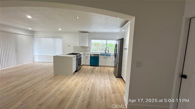 kitchen with appliances with stainless steel finishes, a sink, light wood finished floors, recessed lighting, and white cabinetry