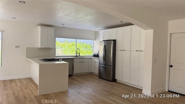 kitchen featuring a peninsula, light wood-type flooring, a textured ceiling, a sink, and stainless steel appliances