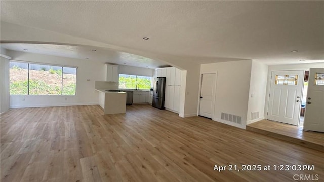 unfurnished living room with arched walkways, baseboards, visible vents, and light wood-type flooring