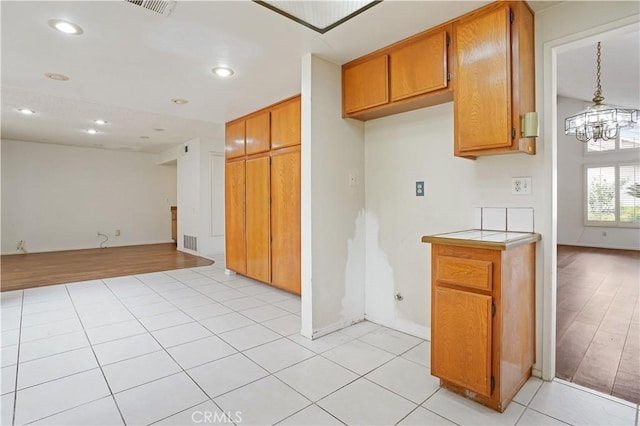 kitchen with brown cabinetry, light countertops, open floor plan, an inviting chandelier, and recessed lighting