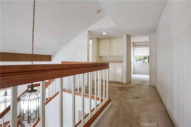 corridor with an upstairs landing, a textured ceiling, and light colored carpet