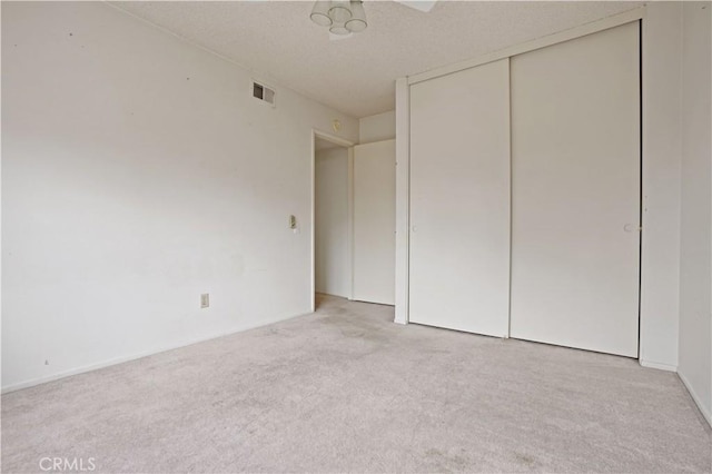 unfurnished bedroom with carpet floors, a textured ceiling, visible vents, and a closet