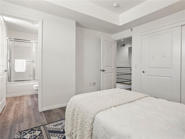 bedroom featuring connected bathroom, baseboards, wood finished floors, and a closet