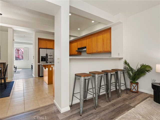 kitchen with wood finished floors, stainless steel fridge, a breakfast bar, under cabinet range hood, and recessed lighting