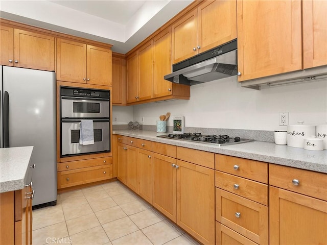 kitchen with under cabinet range hood, stainless steel appliances, light stone countertops, and brown cabinetry