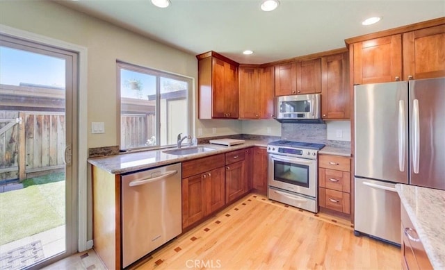 kitchen with brown cabinetry, appliances with stainless steel finishes, light wood-type flooring, a sink, and recessed lighting