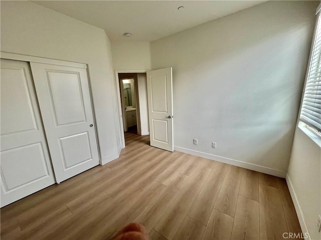 unfurnished bedroom featuring baseboards, a closet, and light wood-type flooring