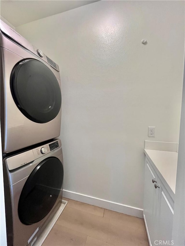washroom with baseboards, cabinet space, and stacked washer / dryer