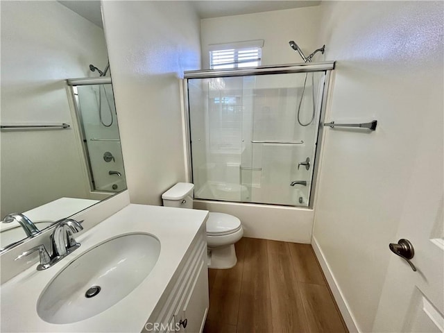 bathroom with shower / bath combination with glass door, toilet, wood finished floors, and vanity