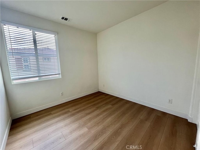 empty room with baseboards, visible vents, and wood finished floors