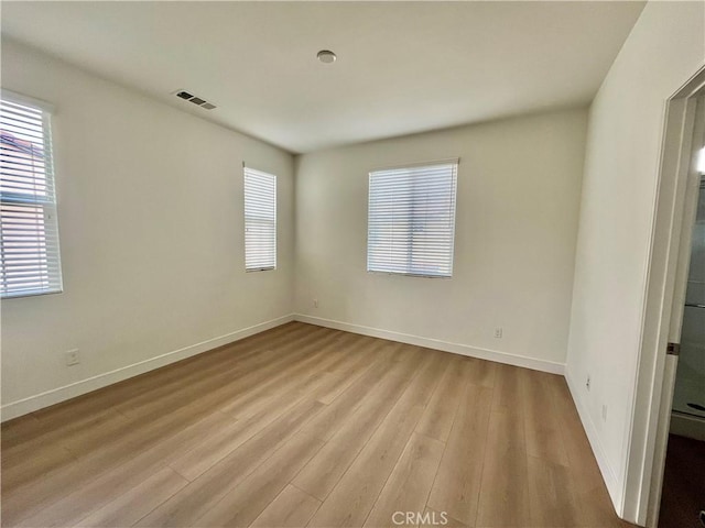 spare room with baseboards, light wood-type flooring, and visible vents