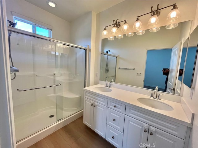 bathroom featuring double vanity, a shower stall, a sink, and wood finished floors