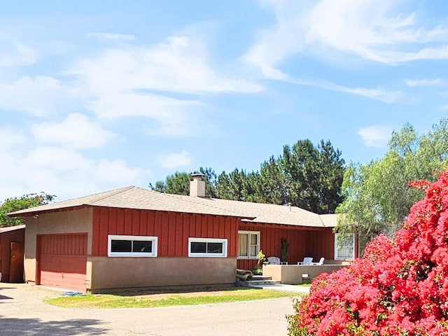single story home featuring a garage, a shingled roof, board and batten siding, and a chimney