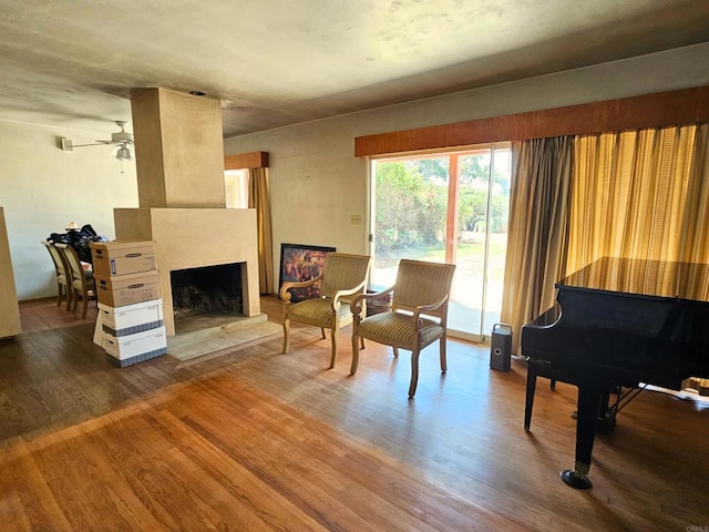 living area with a ceiling fan, a fireplace with raised hearth, and wood finished floors