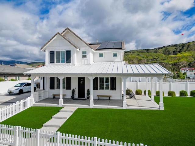 view of front of property with a porch, a front lawn, roof mounted solar panels, and fence private yard
