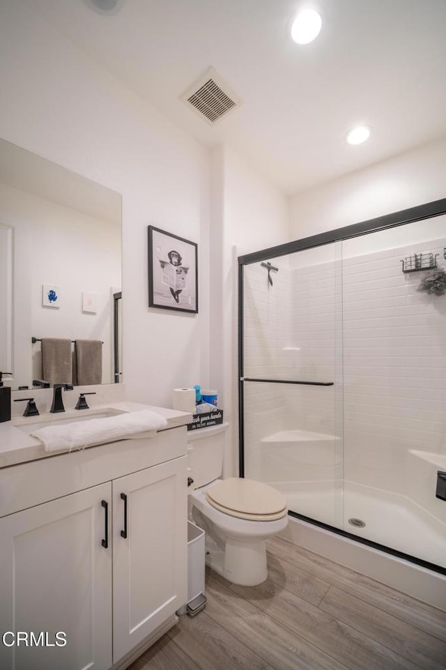 full bath with vanity, toilet, a shower stall, wood finished floors, and visible vents