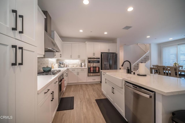 kitchen featuring white cabinetry, appliances with stainless steel finishes, a sink, and wall chimney exhaust hood