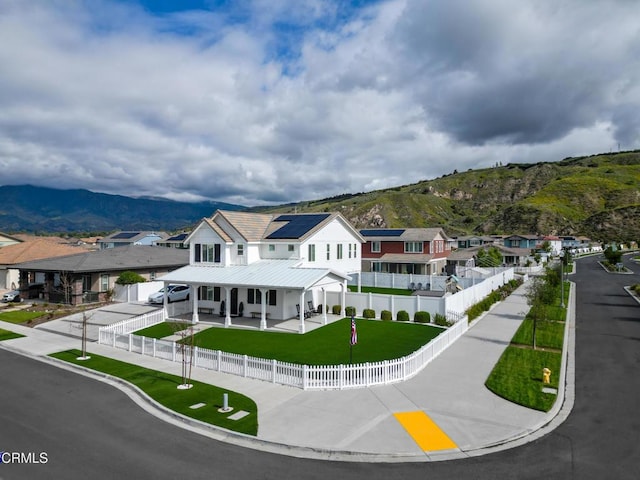 rear view of property featuring covered porch, a lawn, roof mounted solar panels, a mountain view, and a fenced backyard