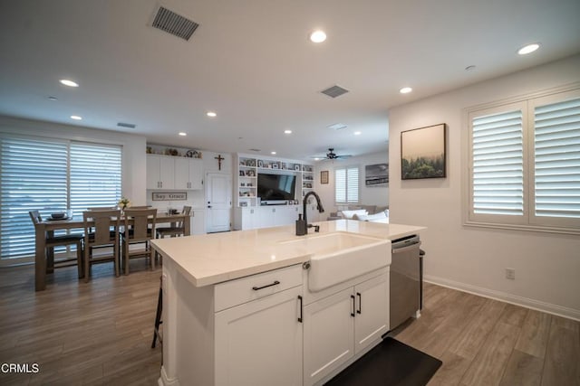 kitchen with a sink, white cabinetry, wood finished floors, stainless steel dishwasher, and visible vents