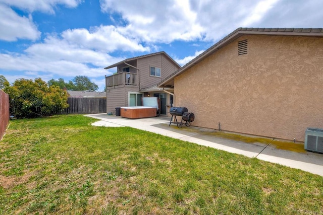 back of house with a hot tub, a fenced backyard, a balcony, a lawn, and a patio