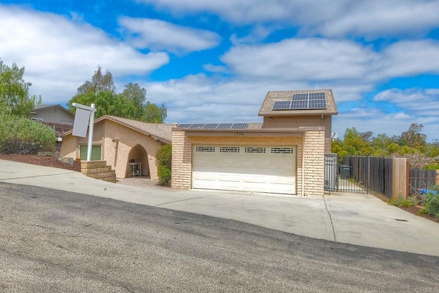 view of front of house featuring fence, an attached garage, brick siding, solar panels, and driveway