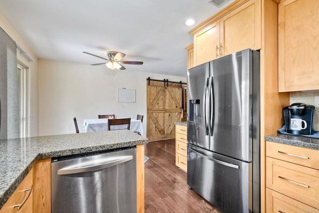 kitchen with appliances with stainless steel finishes, a barn door, light brown cabinets, a ceiling fan, and dark wood-type flooring